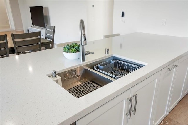 interior details featuring white cabinetry, light stone counters, a sink, and light wood-type flooring