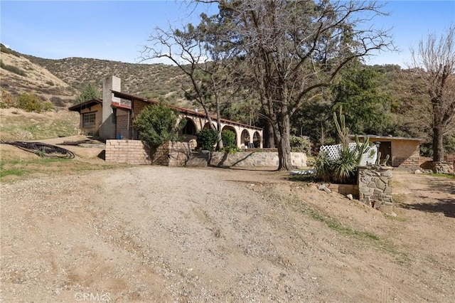 view of front of house featuring dirt driveway, a chimney, and a mountain view