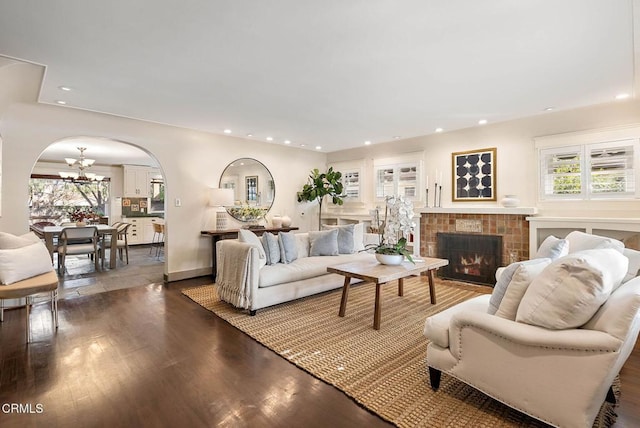 living room with arched walkways, a fireplace, recessed lighting, an inviting chandelier, and wood finished floors