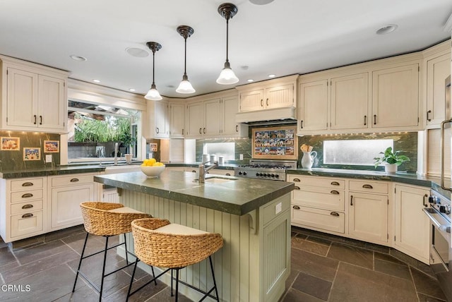 kitchen with dark countertops, stone tile flooring, under cabinet range hood, and cream cabinets