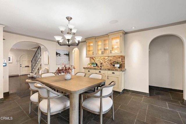 dining room with arched walkways, a notable chandelier, stone tile floors, ornamental molding, and stairs