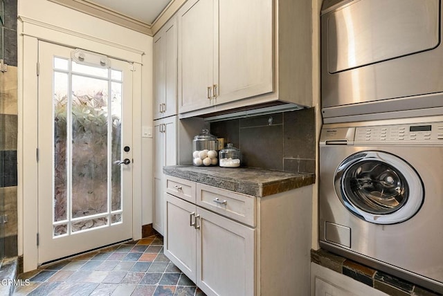 laundry room featuring stacked washing maching and dryer, stone finish floor, and cabinet space