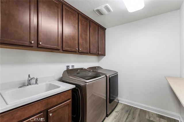 laundry area with cabinet space, visible vents, light wood-style flooring, washing machine and clothes dryer, and a sink