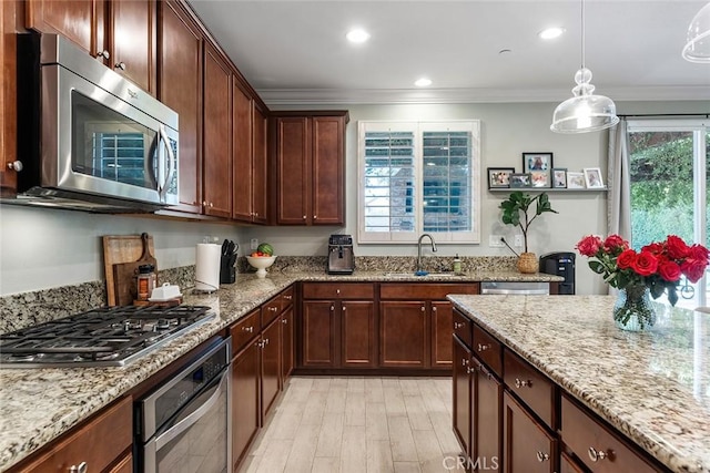 kitchen with crown molding, stainless steel appliances, a sink, light stone countertops, and pendant lighting