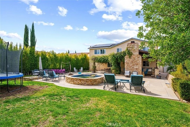 exterior space featuring a patio, a trampoline, stucco siding, and an in ground hot tub