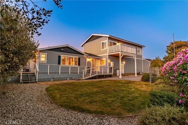 rear view of house with a balcony, fence, a patio, and a yard