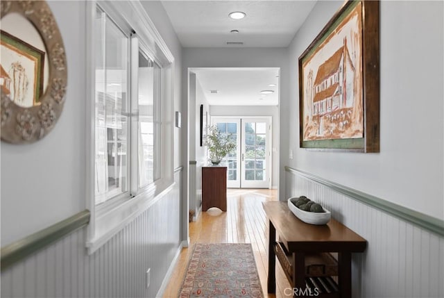 hallway featuring a wainscoted wall, visible vents, and light wood finished floors