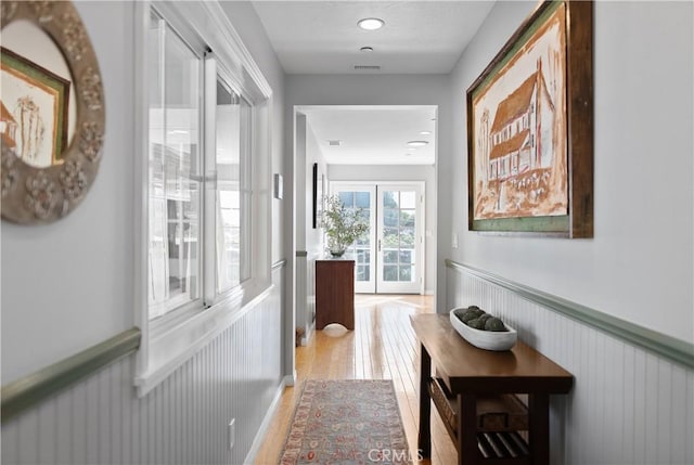 hall with light wood-style flooring, visible vents, and wainscoting