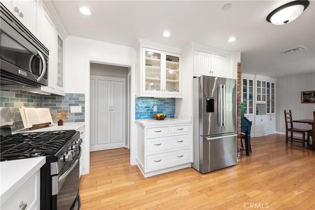 kitchen featuring range with gas stovetop, white cabinets, light countertops, and stainless steel refrigerator with ice dispenser