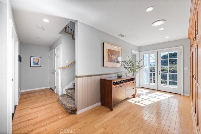 foyer entrance featuring a wainscoted wall, stairs, french doors, light wood finished floors, and recessed lighting