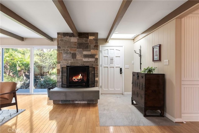 living area featuring beam ceiling, baseboards, light wood-style floors, and a fireplace