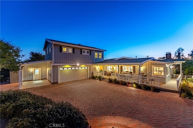 exterior space with covered porch, decorative driveway, a chimney, and board and batten siding