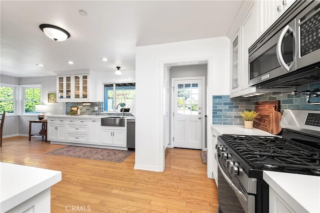 kitchen featuring white cabinetry, light countertops, stainless steel appliances, a sink, and light wood finished floors