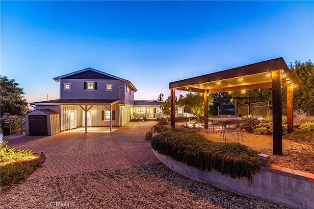 back of property at dusk featuring a shed, decorative driveway, and an outdoor structure
