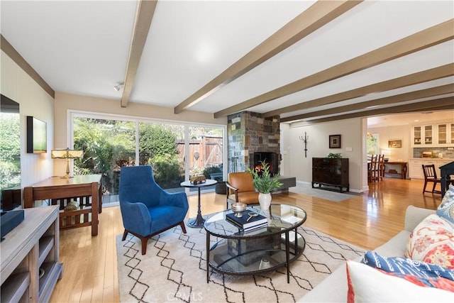 living area featuring light wood finished floors, beamed ceiling, and a stone fireplace