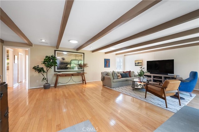 living area featuring beam ceiling, hardwood / wood-style flooring, and baseboards