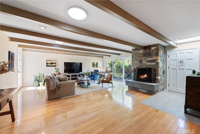 living room featuring light wood finished floors, a stone fireplace, and beam ceiling