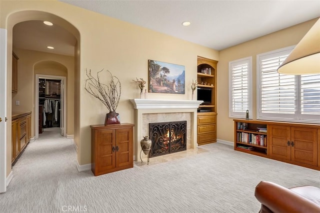 living area featuring arched walkways, light colored carpet, a premium fireplace, baseboards, and built in features