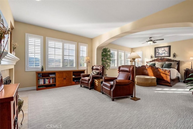 carpeted bedroom with baseboards, arched walkways, ceiling fan, and a glass covered fireplace