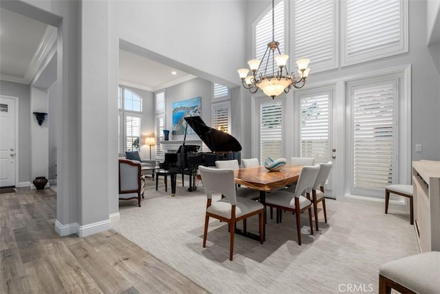 dining area featuring a notable chandelier, a towering ceiling, baseboards, ornamental molding, and light wood finished floors