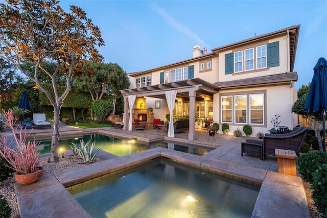 back of house featuring an in ground hot tub, a fireplace, stucco siding, a chimney, and a patio area