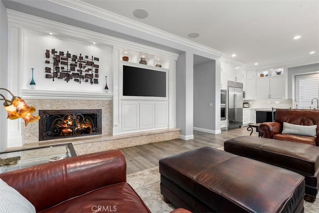 living room with a high end fireplace, crown molding, light wood-style flooring, and recessed lighting