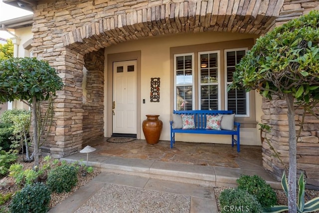 entrance to property with stone siding, a porch, and stucco siding