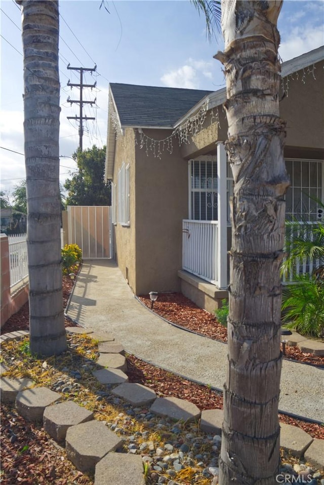 view of side of home featuring a shingled roof, fence, and stucco siding