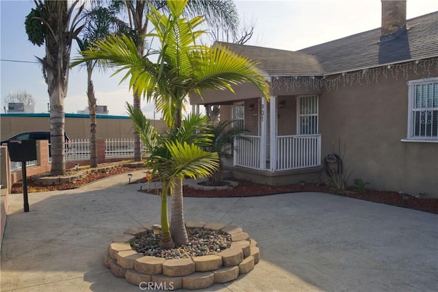 entrance to property featuring a shingled roof, covered porch, fence, and stucco siding