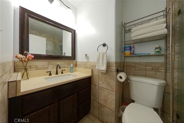 bathroom with toilet, vanity, tile walls, and wainscoting