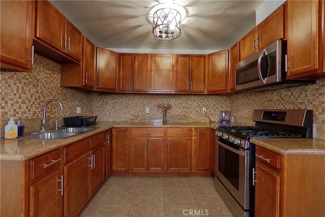 kitchen with brown cabinets, light tile patterned floors, backsplash, appliances with stainless steel finishes, and a sink