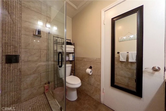 full bath with toilet, tile walls, wainscoting, tile patterned floors, and a stall shower