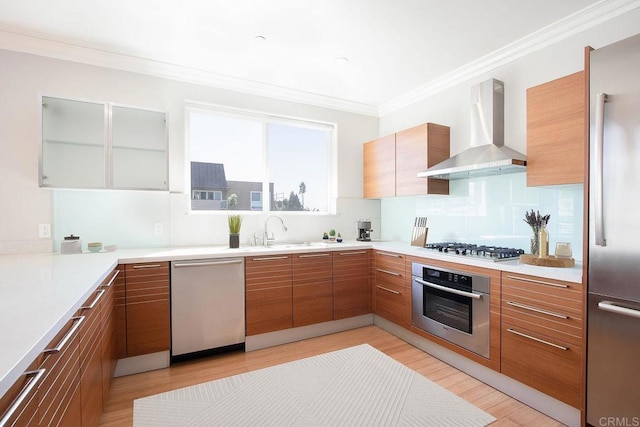 kitchen featuring stainless steel appliances, a sink, wall chimney range hood, brown cabinetry, and modern cabinets