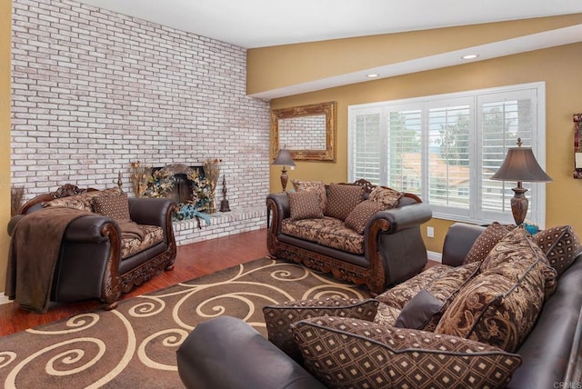 living room with lofted ceiling, a brick fireplace, wood finished floors, and brick wall