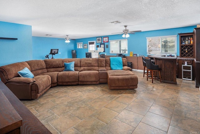 living room featuring visible vents, ceiling fan, a bar, wine cooler, and a textured ceiling