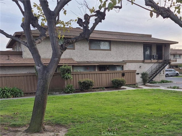 exterior space with stairs, stucco siding, a front yard, and fence