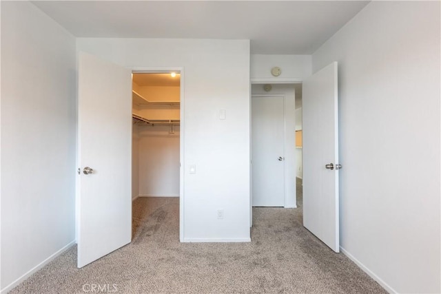 unfurnished bedroom featuring a closet, baseboards, a walk in closet, and carpet