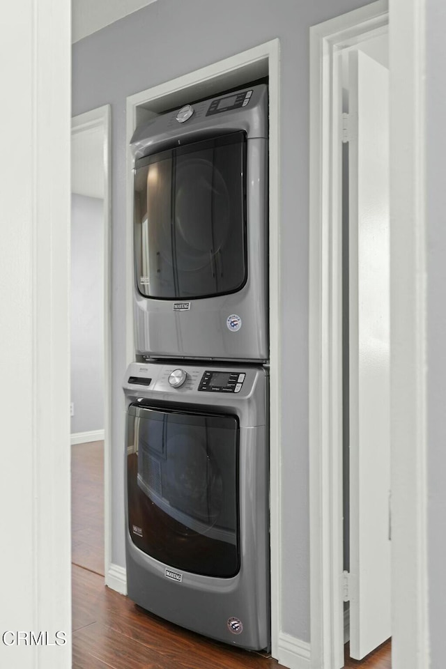 laundry area with laundry area, baseboards, stacked washer / dryer, and wood finished floors