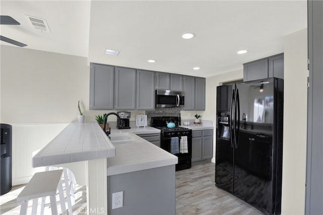 kitchen with a peninsula, black appliances, visible vents, and gray cabinets