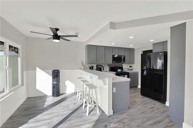 kitchen featuring a peninsula, a kitchen breakfast bar, light countertops, gray cabinets, and black appliances