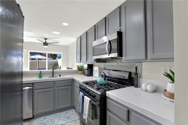 kitchen with tile countertops, decorative backsplash, gray cabinetry, a sink, and black appliances