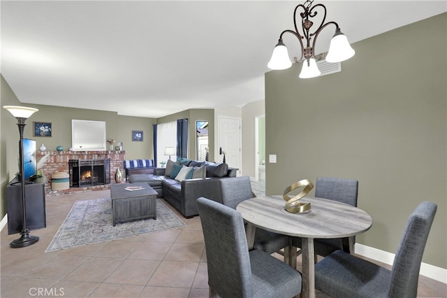 dining room featuring a notable chandelier, light tile patterned flooring, baseboards, and a brick fireplace