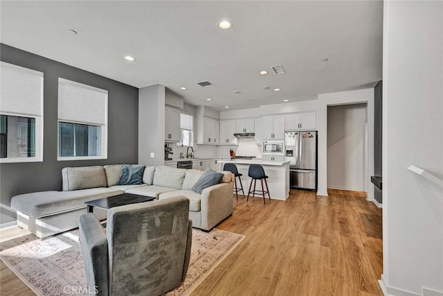 living area featuring light wood-type flooring, baseboards, visible vents, and recessed lighting