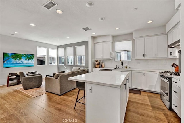 kitchen with visible vents, a breakfast bar area, open floor plan, light wood-style floors, and gas stove