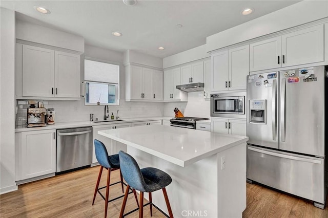 kitchen featuring a breakfast bar area, under cabinet range hood, a sink, light wood-style floors, and appliances with stainless steel finishes