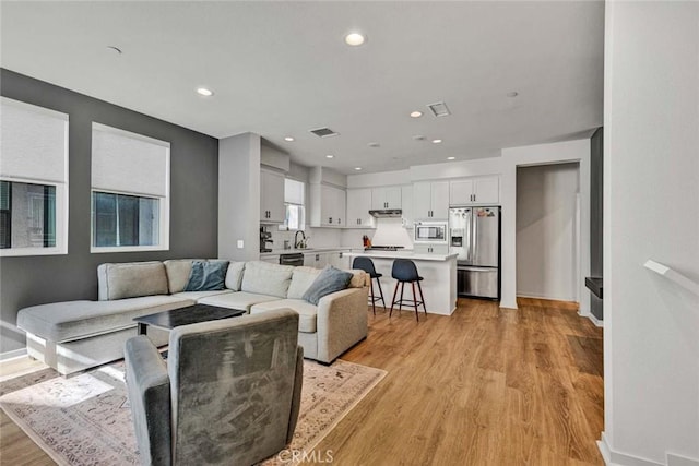 living area with baseboards, light wood-style flooring, visible vents, and recessed lighting