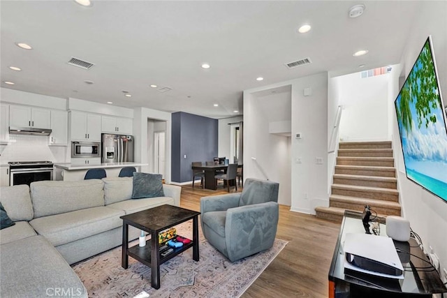 living area featuring recessed lighting, visible vents, light wood finished floors, and stairs