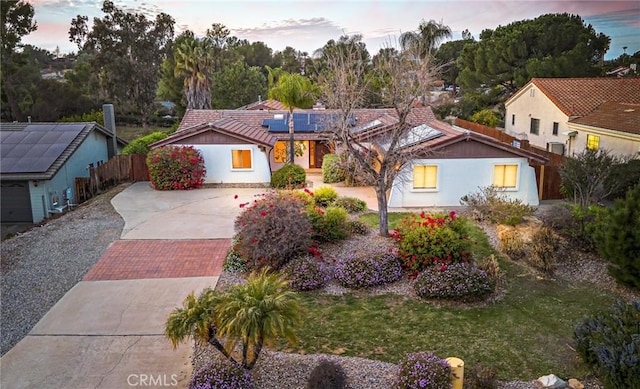 mediterranean / spanish-style home featuring a tile roof, roof mounted solar panels, fence, and a front lawn