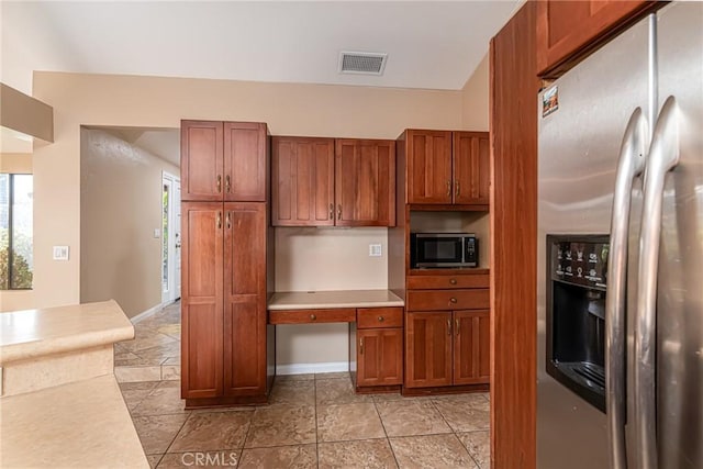 kitchen featuring brown cabinets, visible vents, built in study area, stainless steel fridge, and baseboards