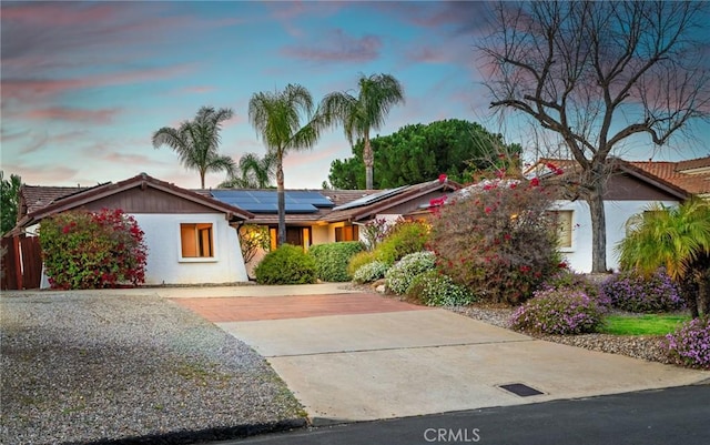 ranch-style home featuring concrete driveway, solar panels, and stucco siding